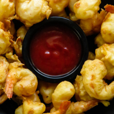 battered and fried shrimp served on a plate with a small bowl of seafodd sauce in the middle.
