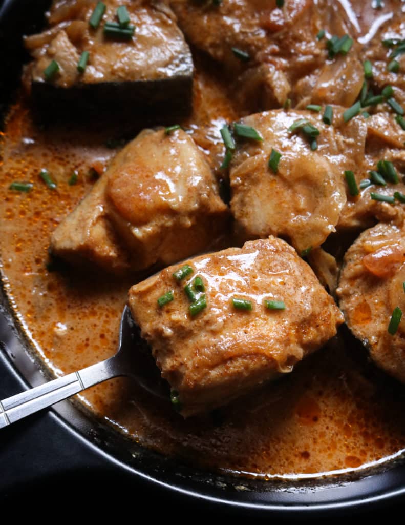 Fish curry serving from a spoon with a gravy and garnished.