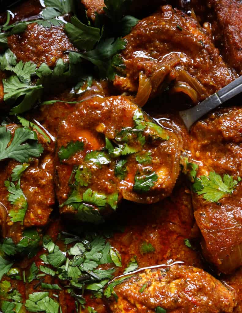 Goan fish currly pieces served from a spoon and garnished with chopped coriander leaves.