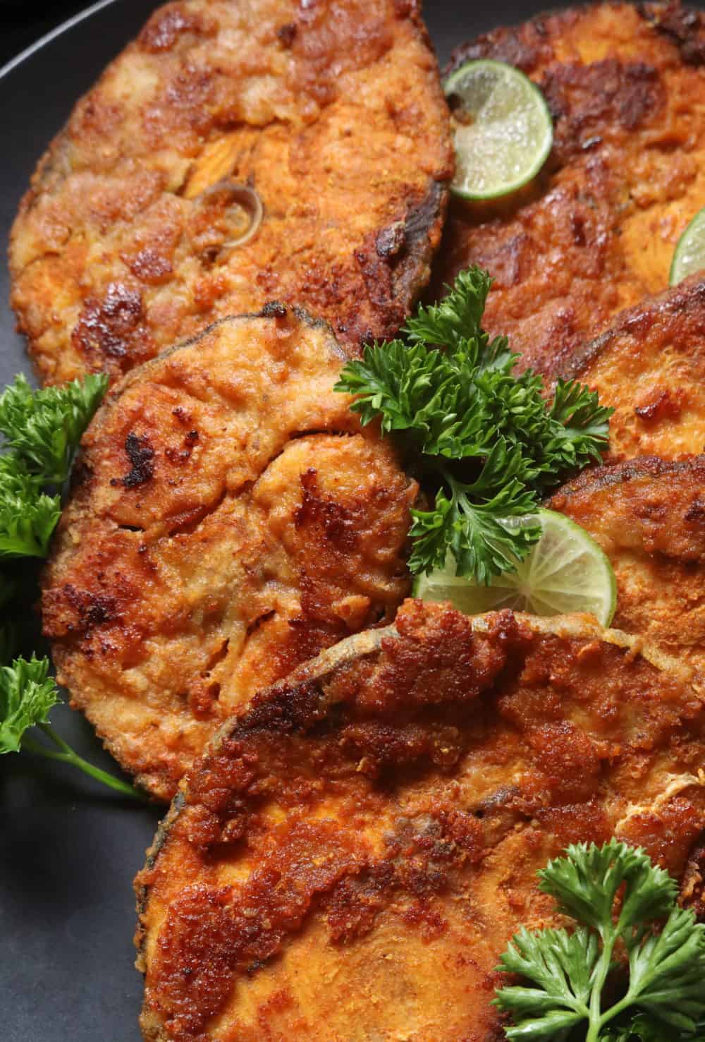 fish fry steaks placed on platter with lime and parsley garnishing.