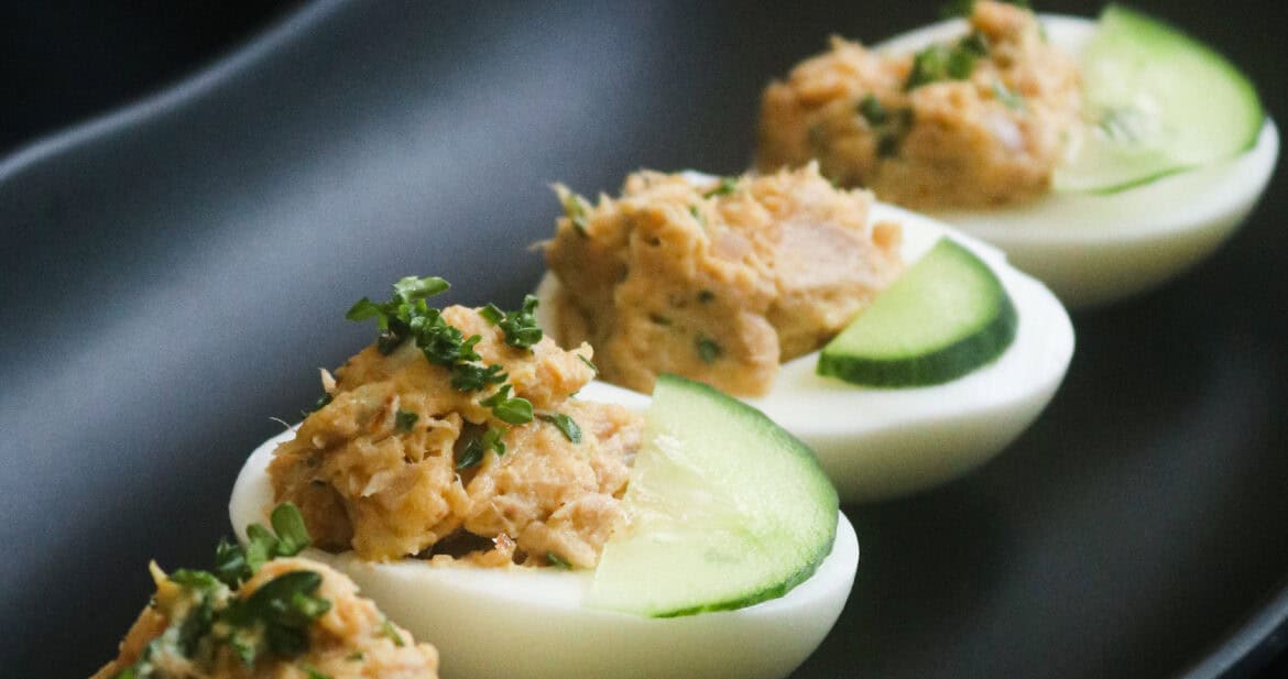 tuna deviled eggs with slices of cucumber and chopped parsley as garnish.